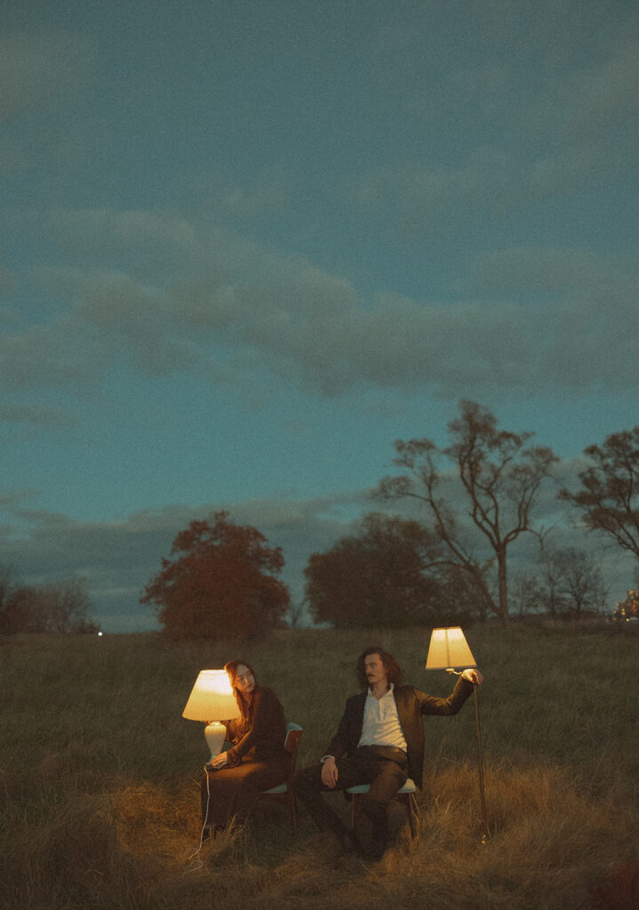 Couple sitting on chairs with lampshades during their outdoor fall engagement session in Detroit, Michigan