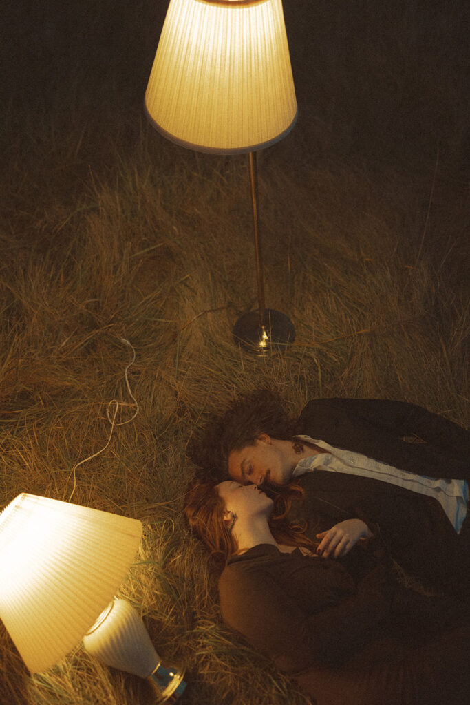 Couple laying in an open field with lampshades during their engagement shoot