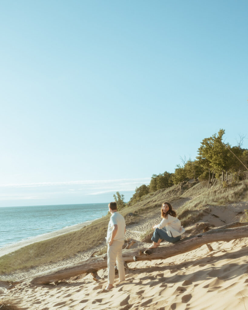 Man and woman sitting on a fallen beach log during their Lake Michigan engagement photos at Duck Lake State Park in Muskegon