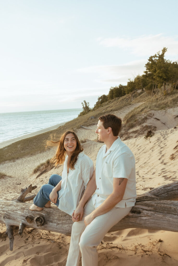 Man and woman sitting on a fallen beach log during their Lake Michigan engagement photos at Duck Lake State Park in Muskegon