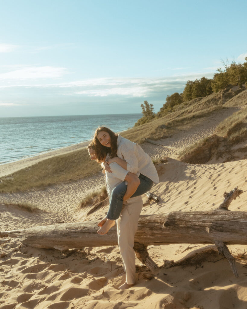 Man giving his fiancé a piggy back ride during their Lake Michigan engagement photos at Duck Lake State Park in Muskegon