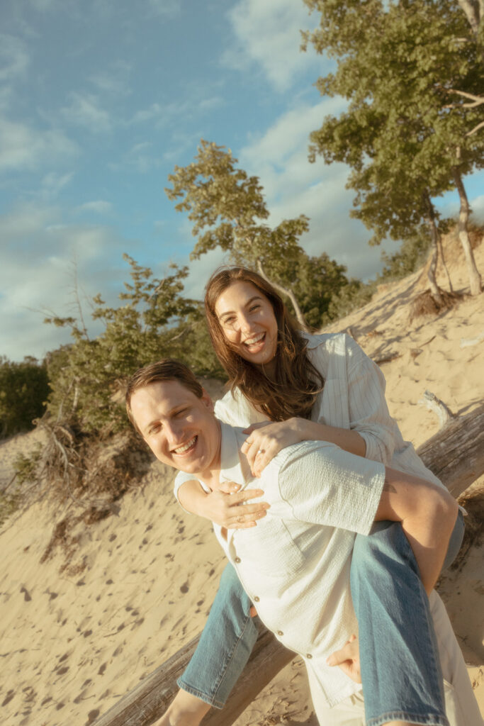 Man giving his fiancé a piggy back ride during their Michigan beach engagement photos in Muskegon