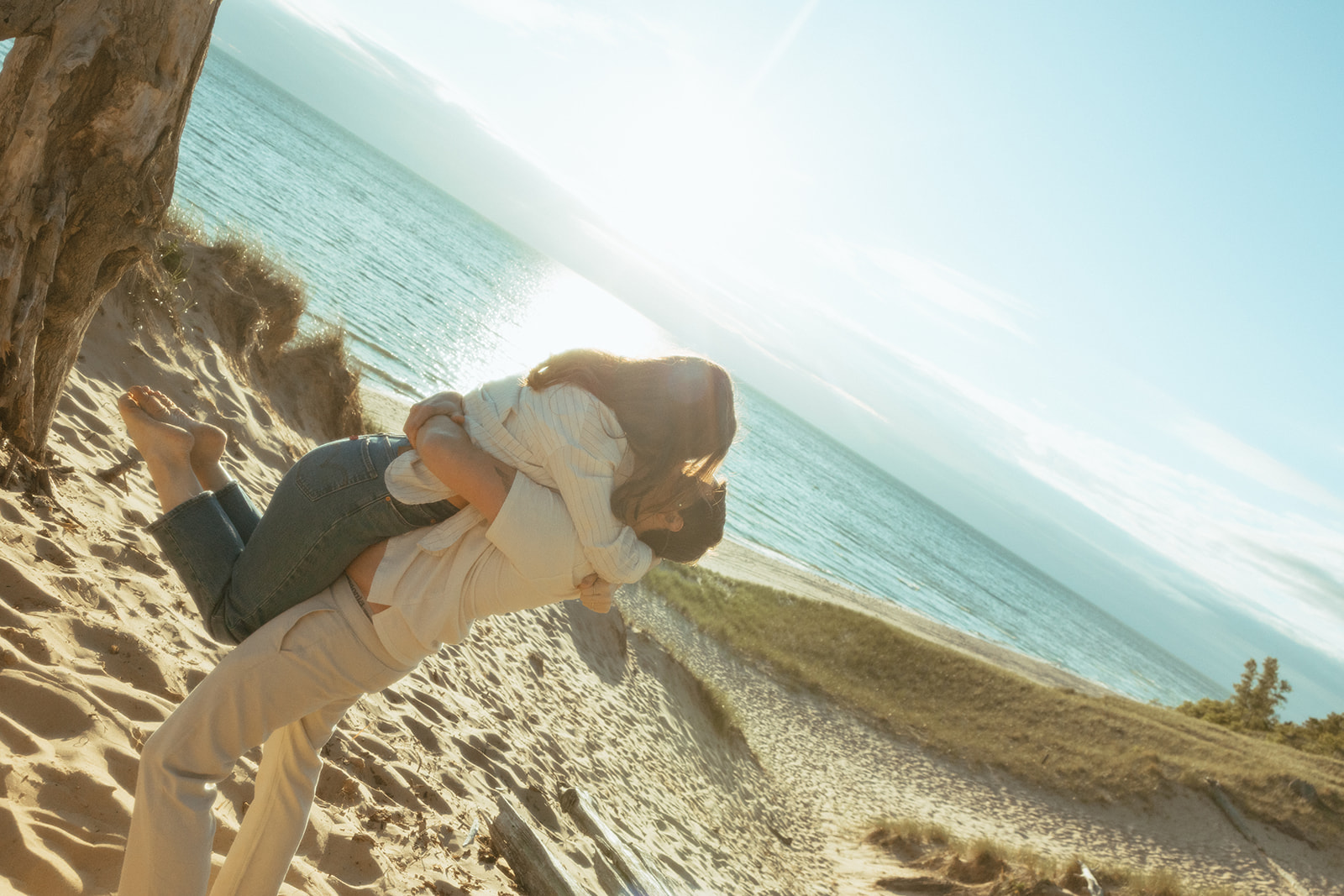 Man picking up his fiancé during their Lake Michigan engagement photos at Duck Lake State Park in Muskegon