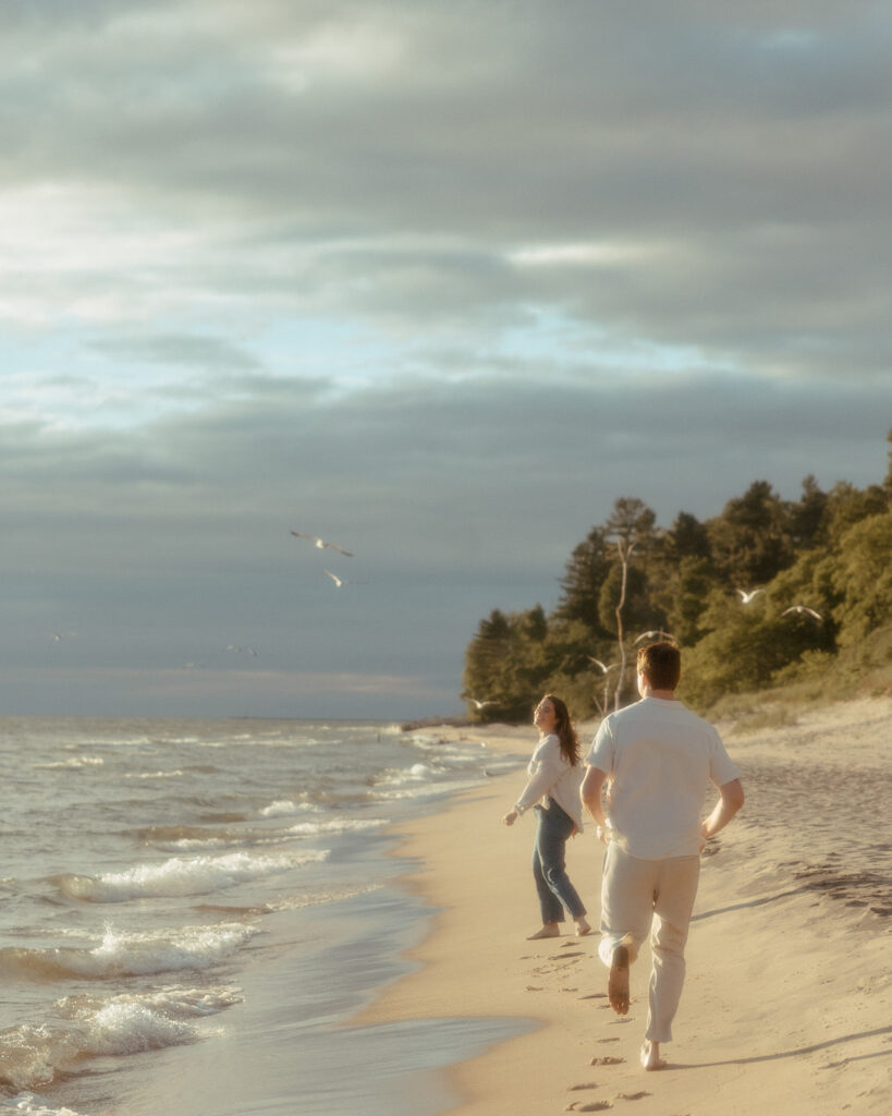 Couple running along the shoreline for their Lake Michigan engagement photos at Duck Lake State Park in Muskegon
