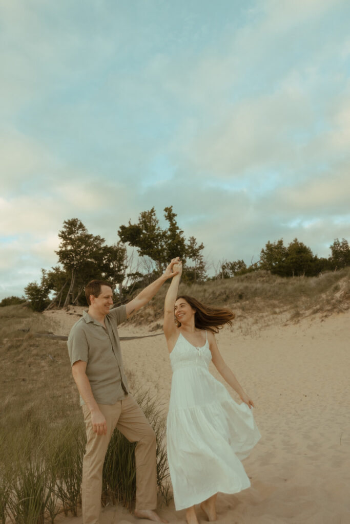 Man twirling his fiancé during their Lake Michigan engagement photos at Duck Lake State Park in Muskegon