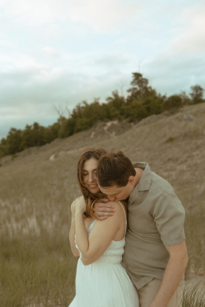 Man kissing his fiancés shoulder during their beach engagement shoot