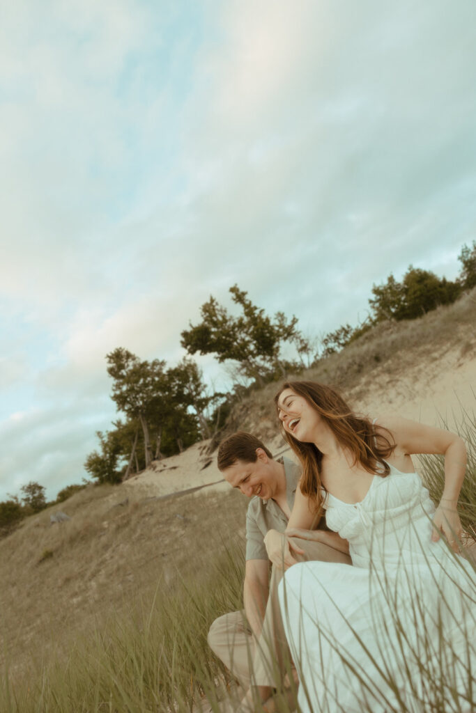 Candid engagement photo of a couple sitting on the beach and laughing