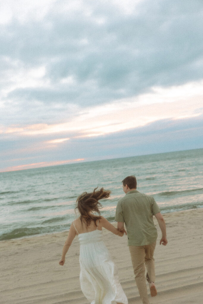 Couple running towards Lake Michigan during their engagement session at Duck Lake State Park in Muskegon