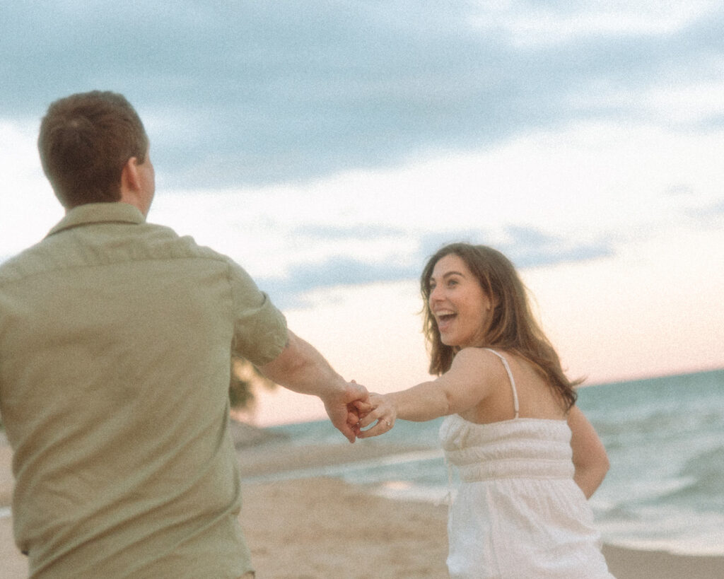 Couple running down the beach for their Lake Michigan engagement photos at Duck Lake State Park in Muskegon