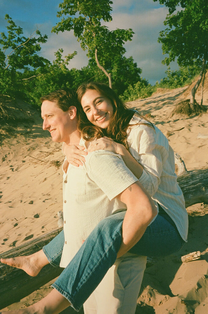 Man giving his fiancé a piggy back ride during their beach engagement session captured on film