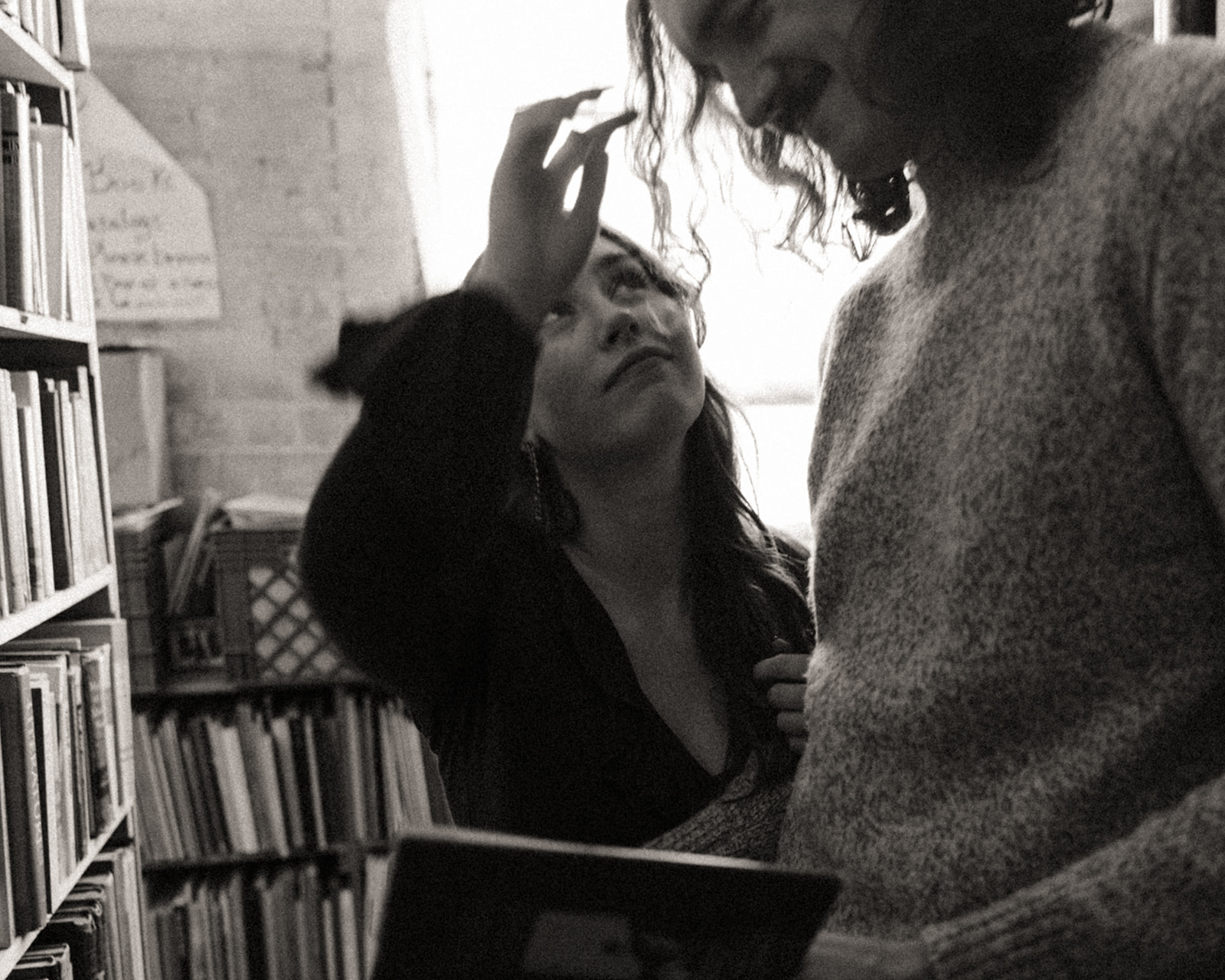 Black and white photo of a woman fixing her fiancés hair during their bookstore engagement session