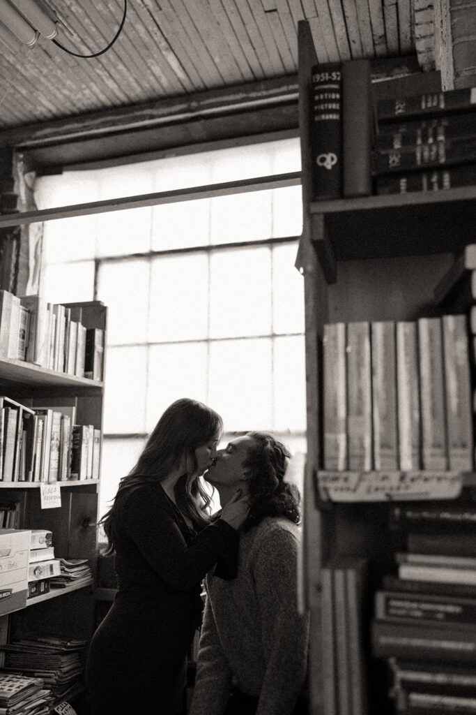 Black and white photo of a couple kissing in a bookstore