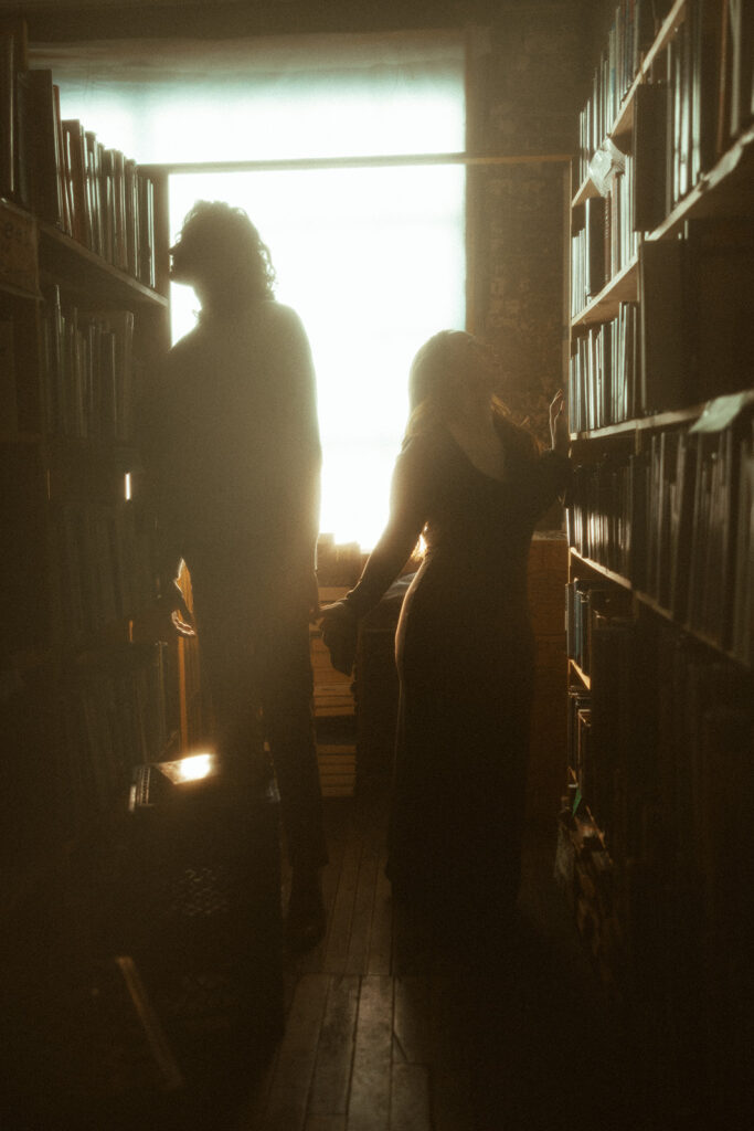 Man and woman holding hands as they look through books during their bookstore engagement session