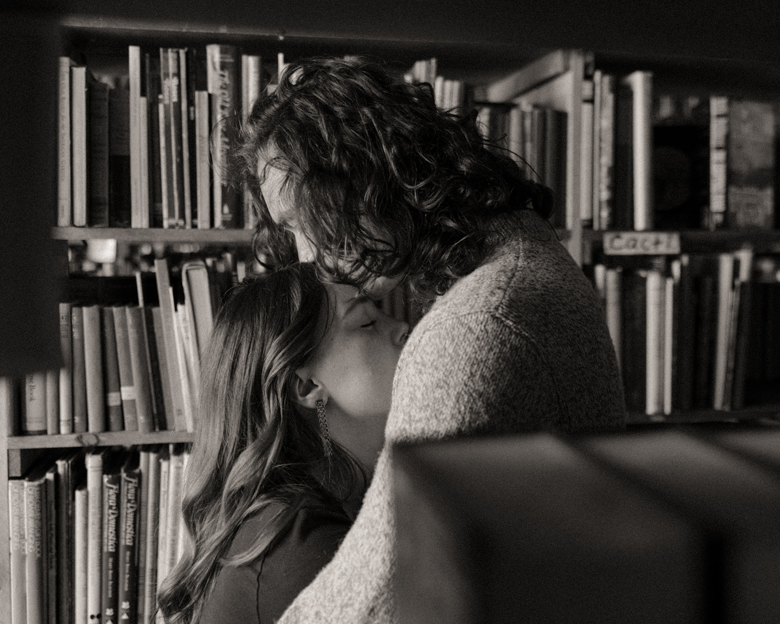 Black and white photo of a man kissing his fiancés head during their bookstore engagement session