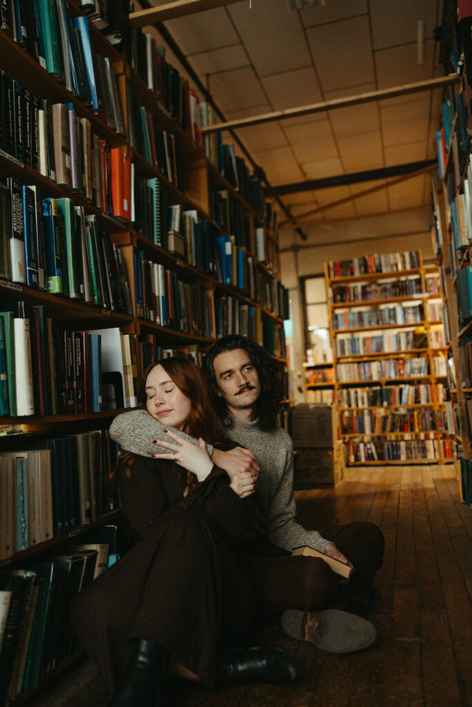 Man and woman sitting on the floor of John K King Books in Detroit, Michigan for their engagement session