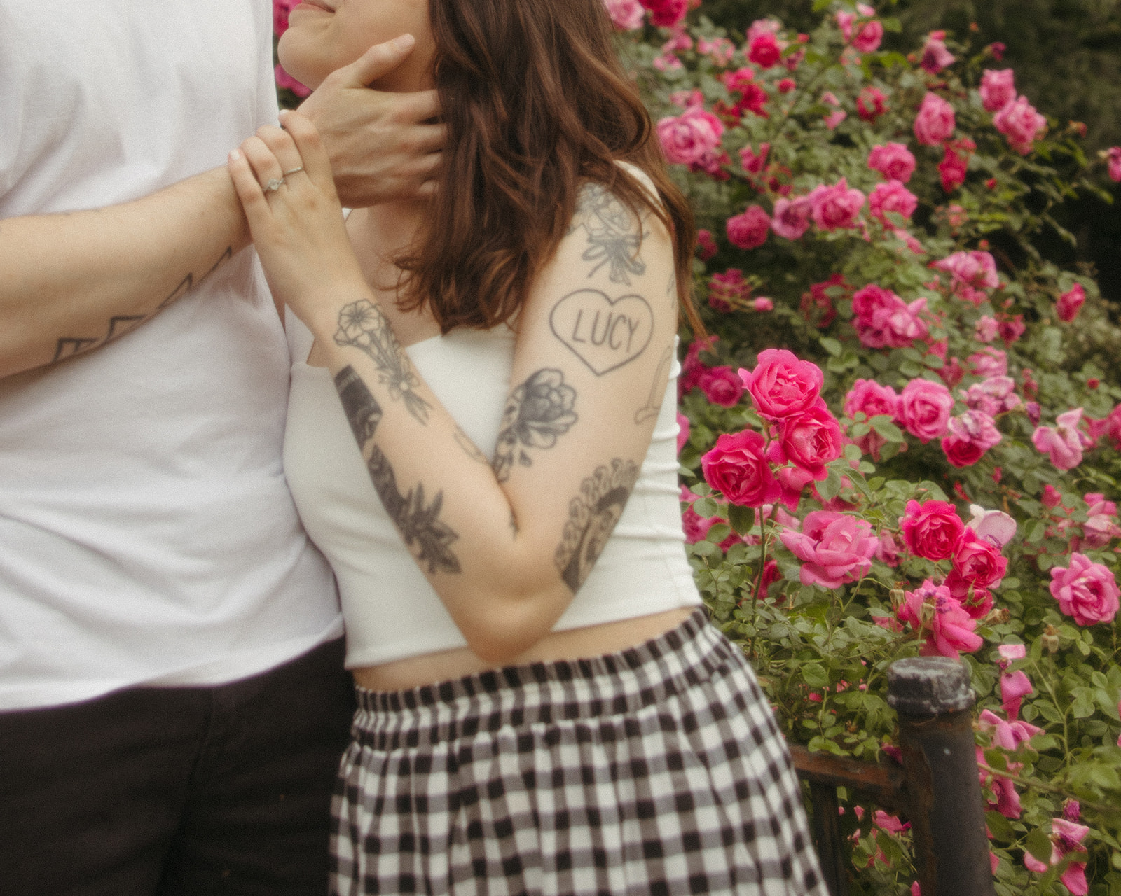 Close up shot of a couple posing in front of a pink rose bush