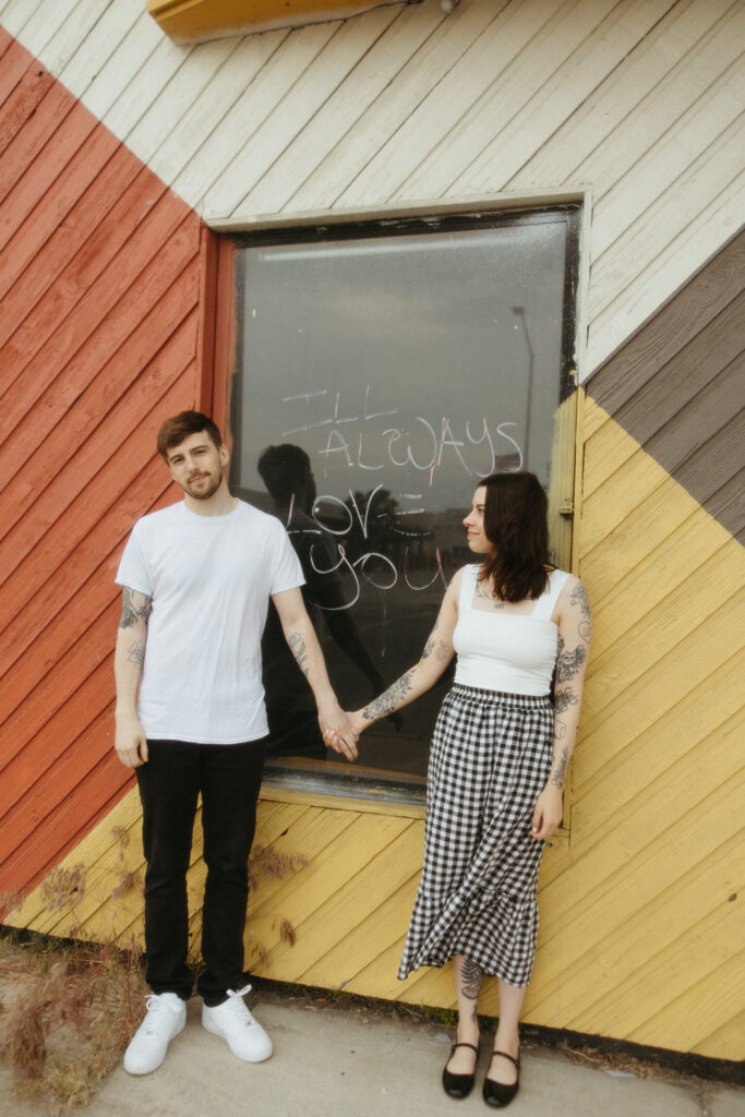 Couple holding hands in front of a window that says "I'll always love you" in downtown Bay City, Michigan