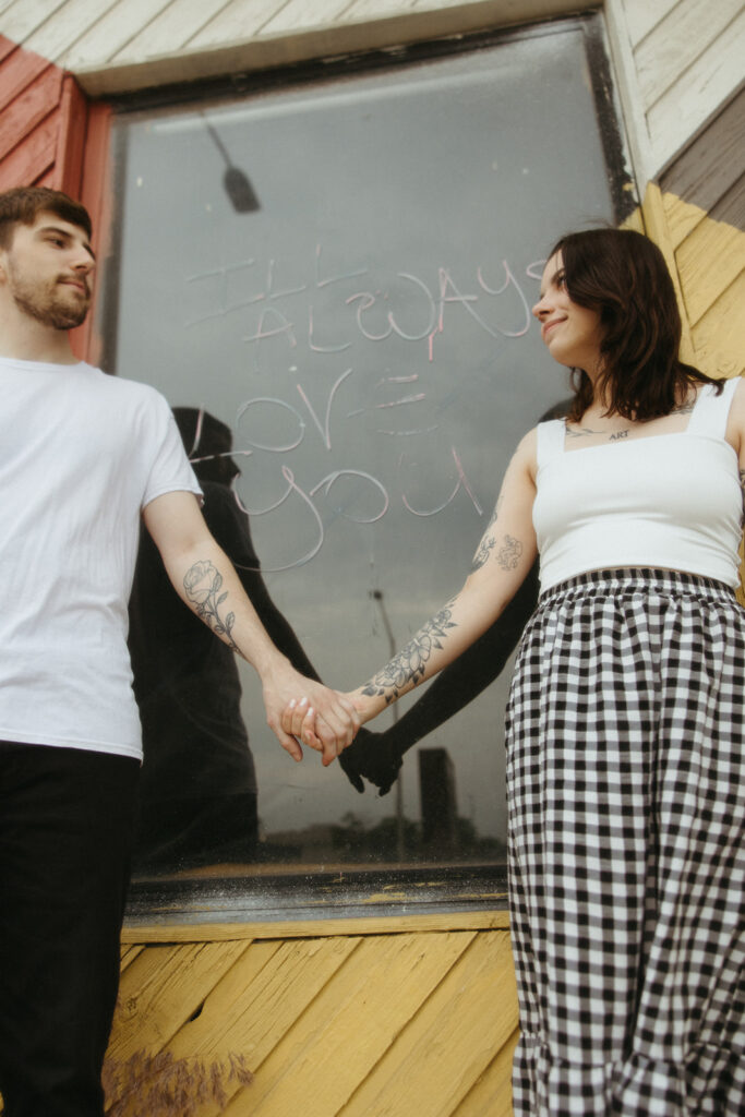 Couple holding hands in front of a window sign that says "I'll always love you"