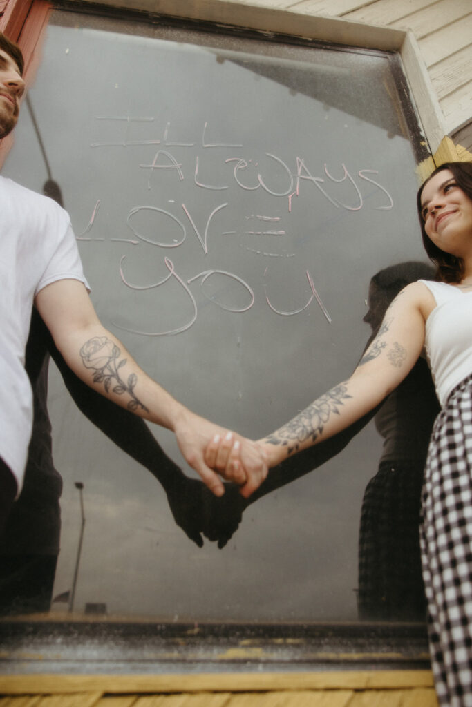 Couple holding hands in front of a window that says "I'll always love you" in downtown Bay City, Michigan