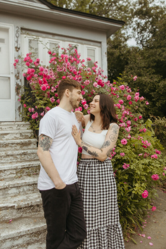 Man and woman posing for their Bay City engagement photos ion front of a rose bush