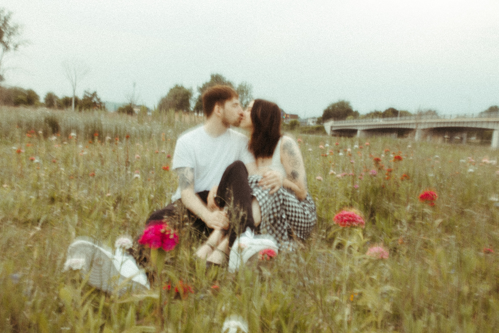 Blurry photo of a couple sitting in a patch of wildflower on the side of a highway for their Bay City Michigan engagement photos