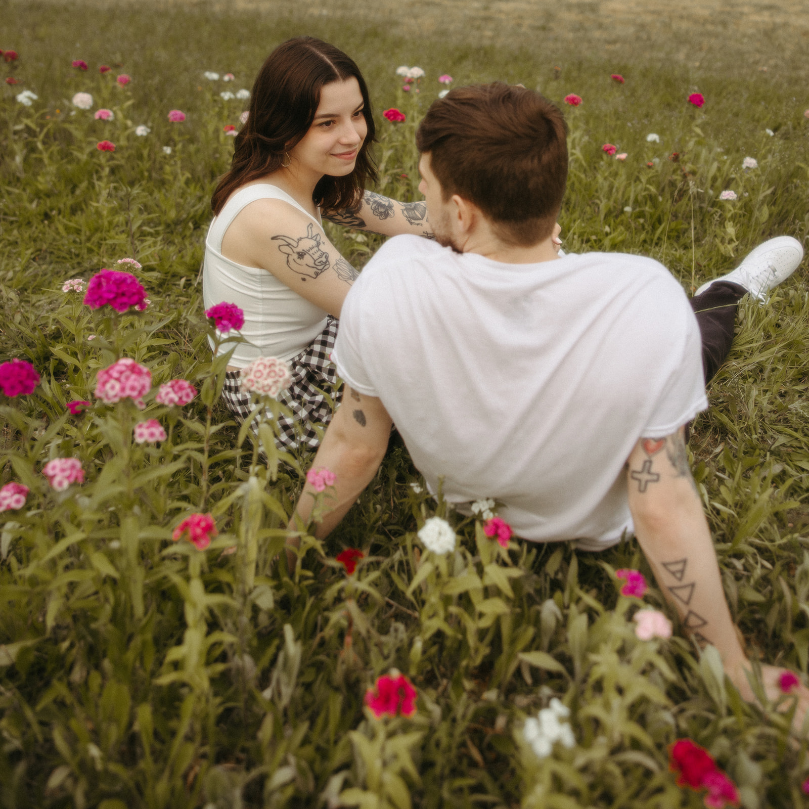 Couple sitting in a patch of wildflowers for their outdoor summer engagement photos in Michigan