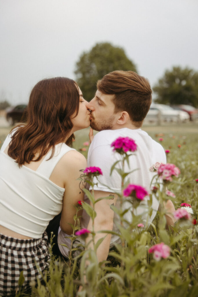 Couple kissing as they sit in a patch of wild flowers