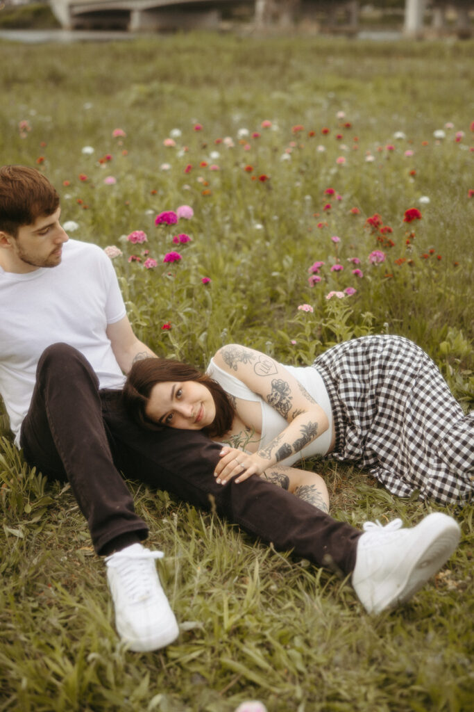 Woman laying on her fiancés leg during their outdoor summer engagement shoot