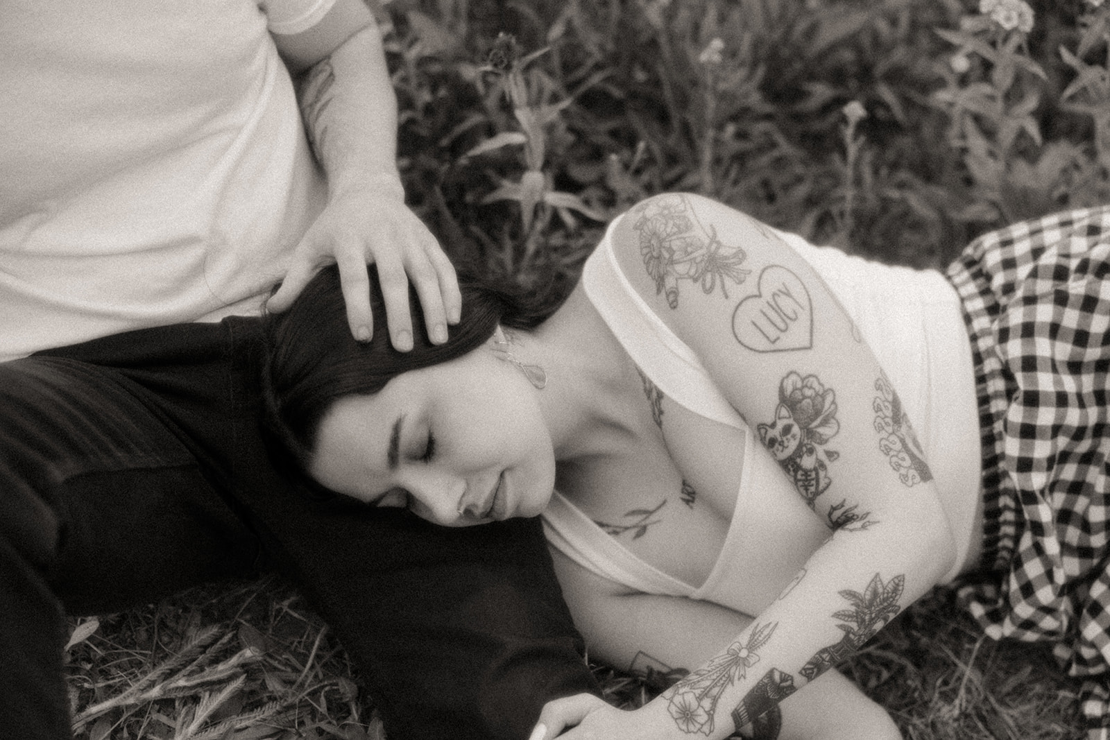 Black and white photo of a woman laying on her fiancés leg