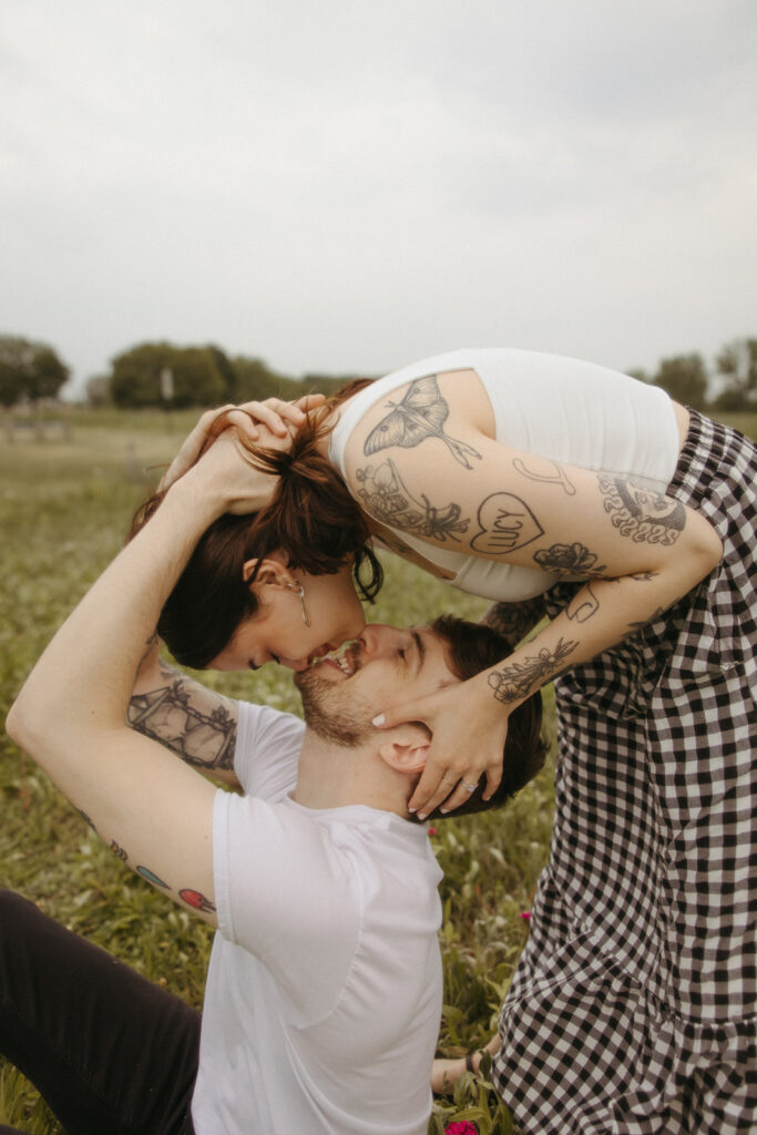 Woman leaning over to kiss her fiancé during their outdoor summer engagement shoot