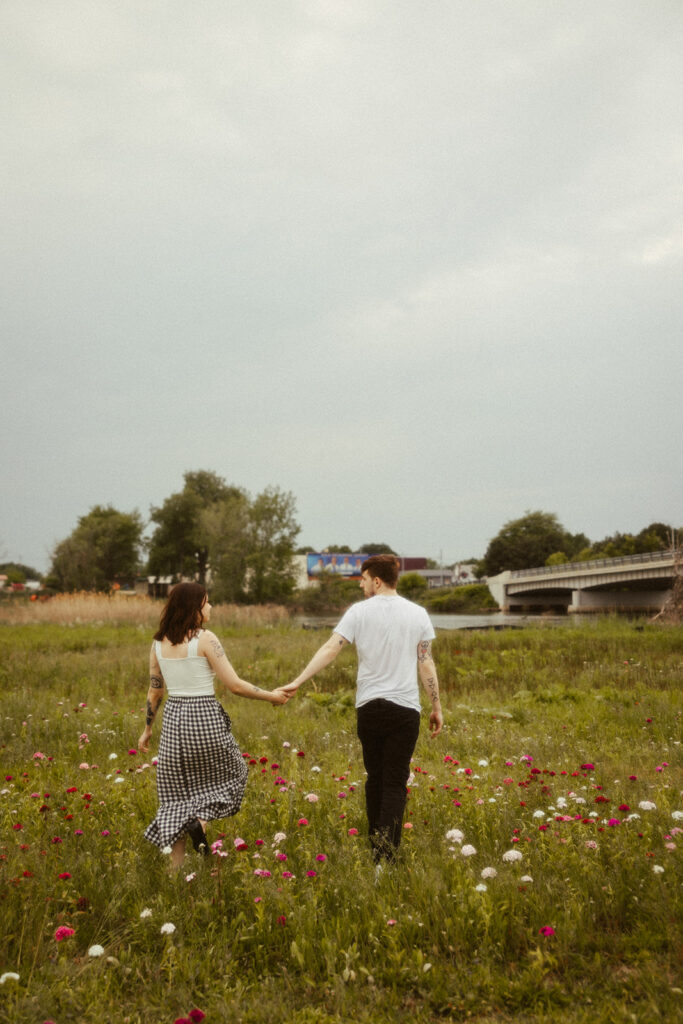 Man and woman holding hands and walking through wildflowers