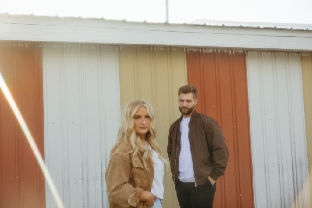 Couple posing for photos outside of a yellow and red barn in the Midwest