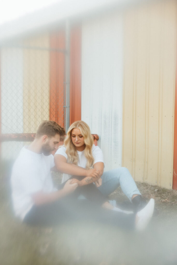 Couple sitting on the ground and holding hands during their outdoor engagement shoot in the Midwest