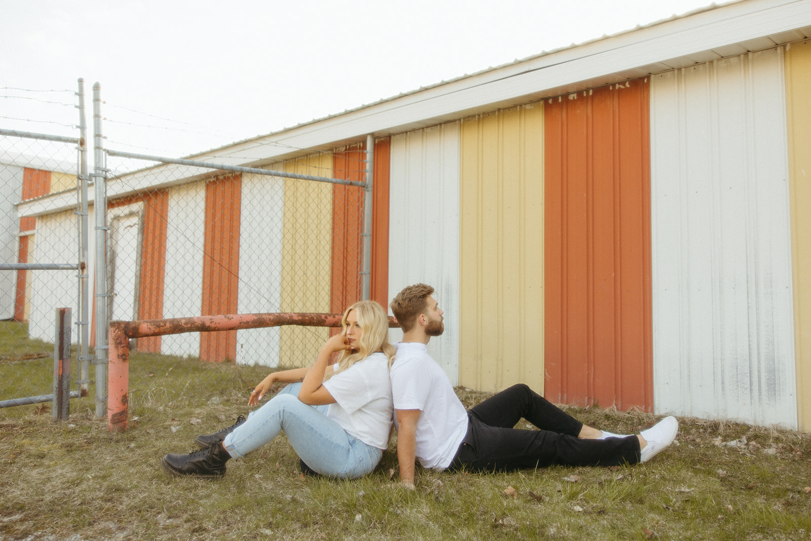 Couple sitting on the ground in front of a yellow and red barn for their Midwest engagement photos