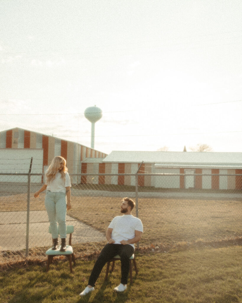 Woman standing on top of a chair during her grunge engagement photoshoot with her partner in the Midwest