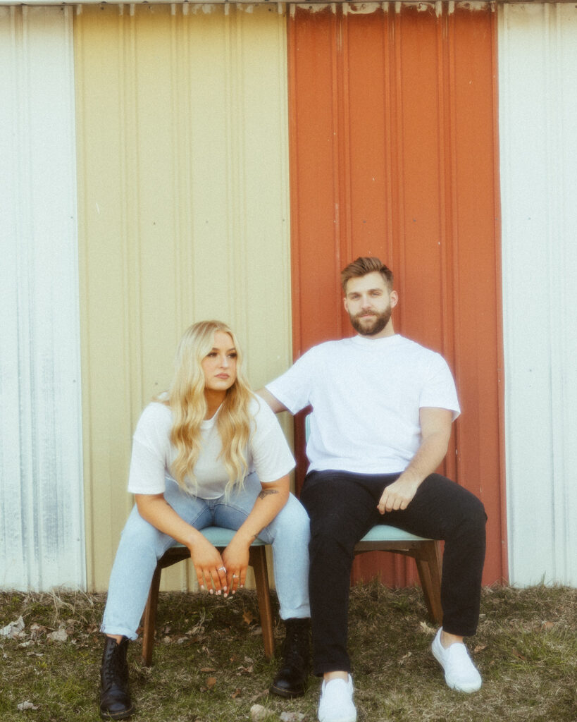 Couple posing in front of a yellow and red barn for their grunge engagement photos in Detroit, Michigan