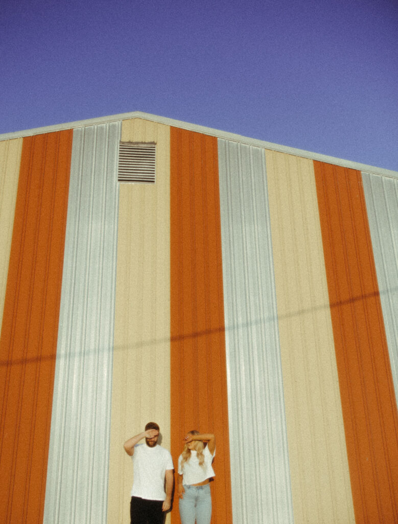 Couple posing in front of a yellow and red barn for their grunge engagement photos in Detroit, Michigan