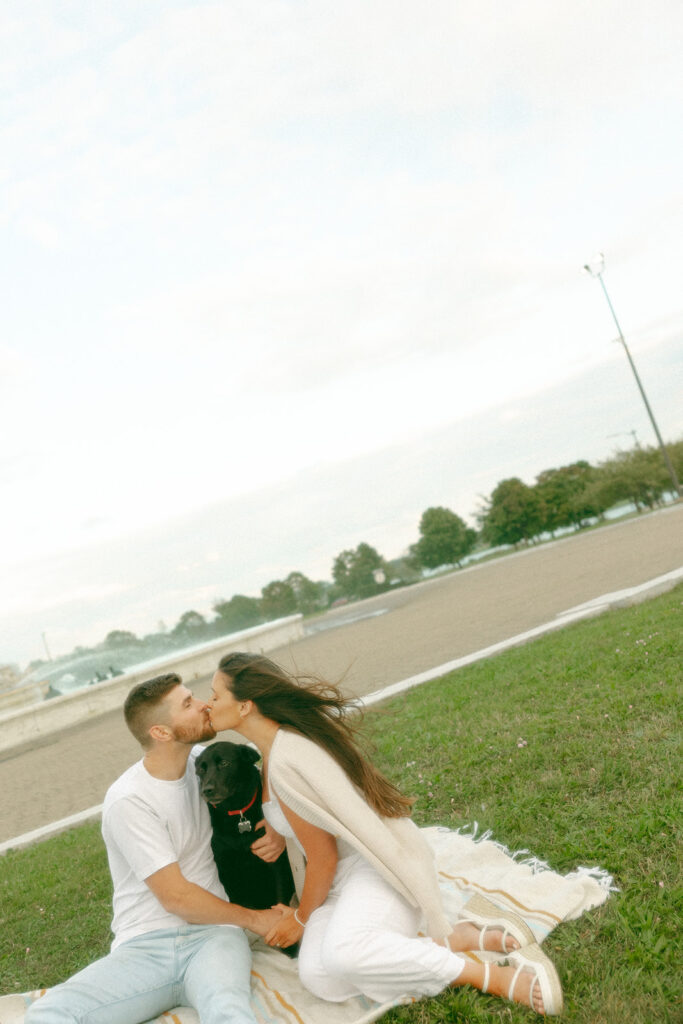 Couple kissing in the grass with their dog at Belle Isle in Detroit, MI