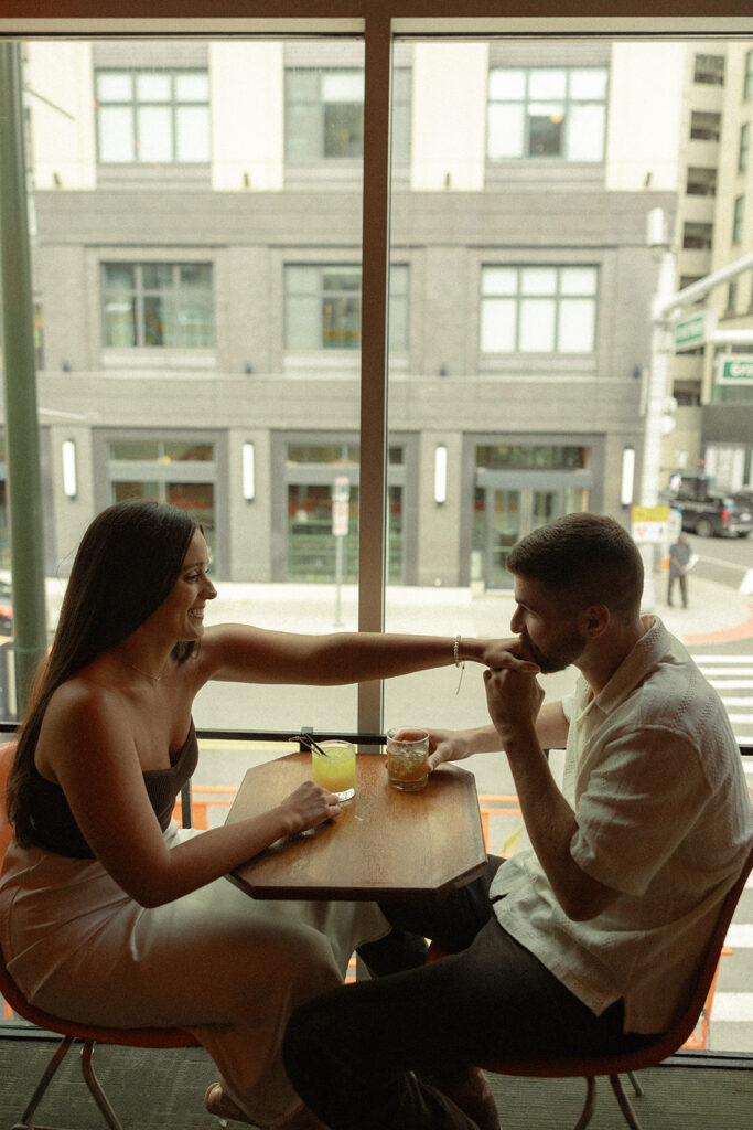 Man kissing his fiancés hand during their bar engagement shoot in downtown Detroit, MI