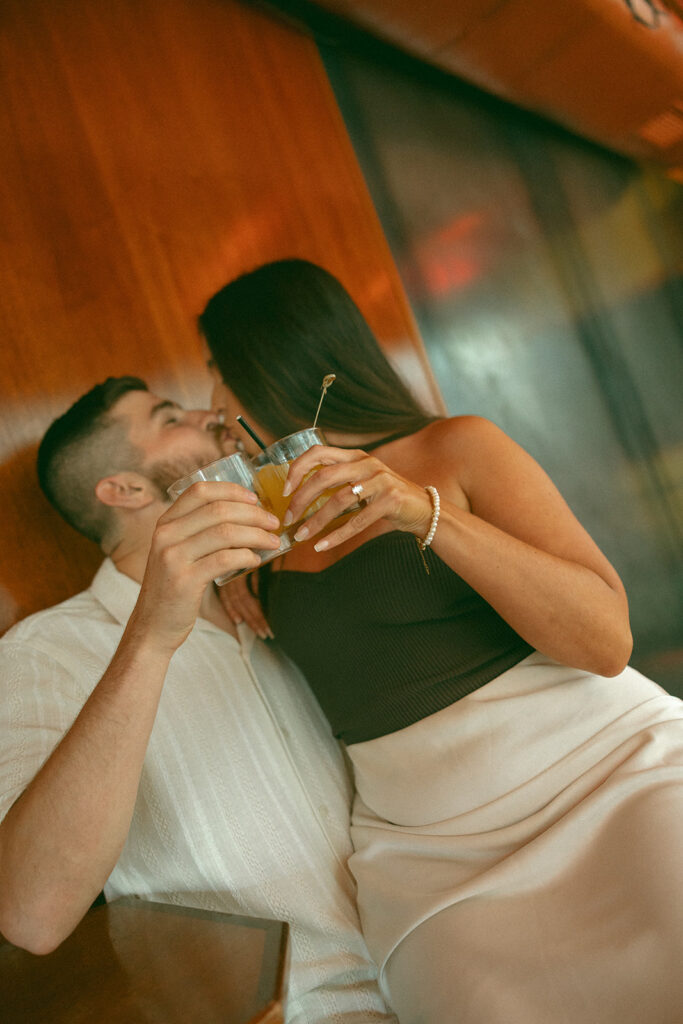 Couple kissing with their drinks during their bar engagement shoot in Detroit, MI