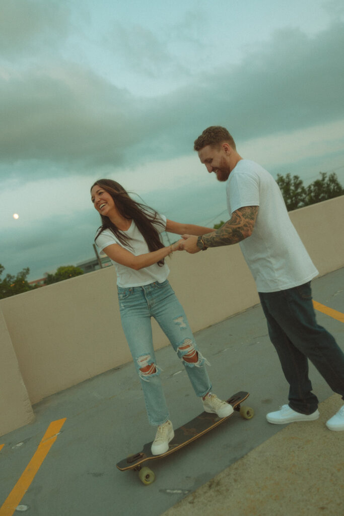 Couple longboarding on a parking garage in Midland, Michigan for their laid-back engagement photos