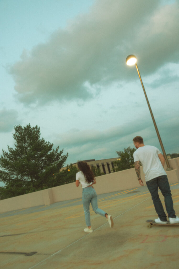 Man longboarding with his fiancé on a rooftop parking garage