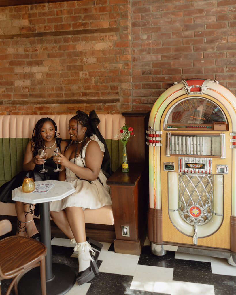 Couple sitting at a table with glasses of champagne for their engagement photos in Detroit at Time Will Tell.