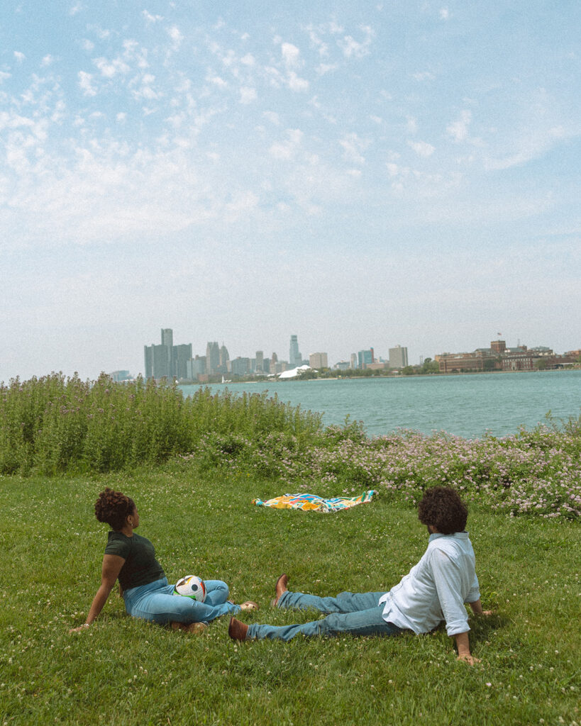 Couple sitting in the grass and admiring the city views of Detroit at Belle Isle.