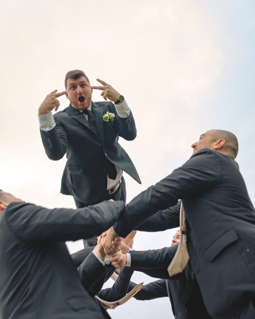 Fun groom and groomsmen portraits of the groomsmen throwing the groom up in the air