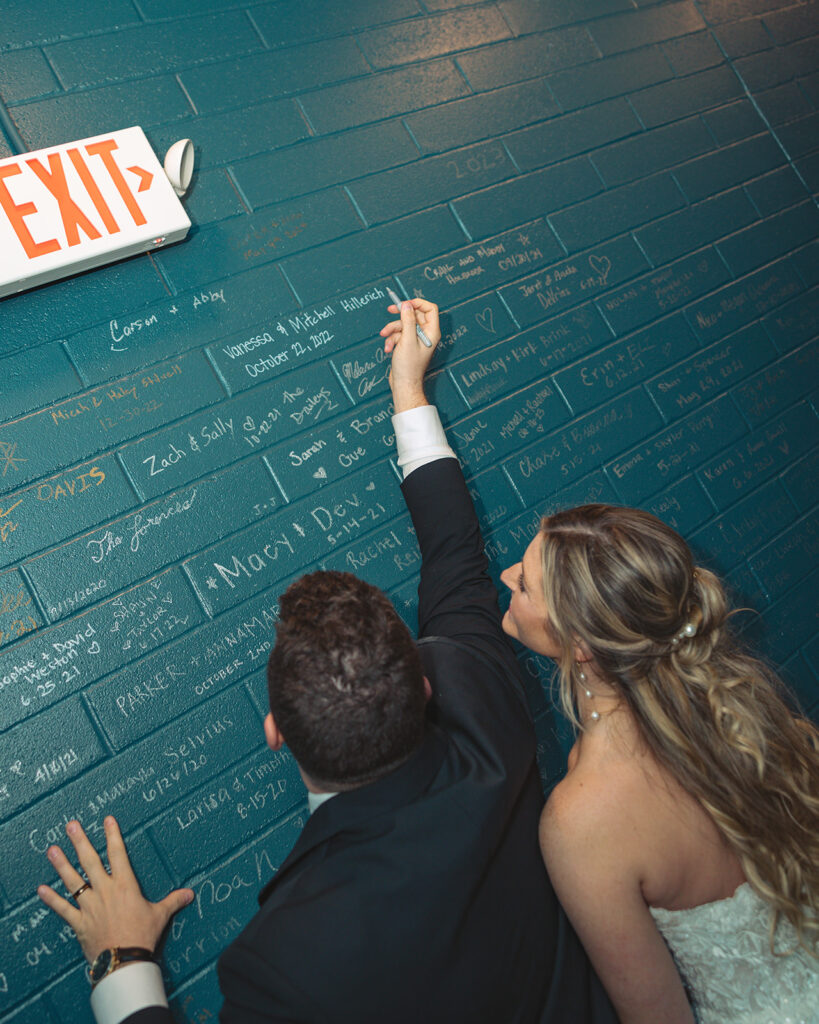 Bride and groom signgin the Port 393 wedding wall