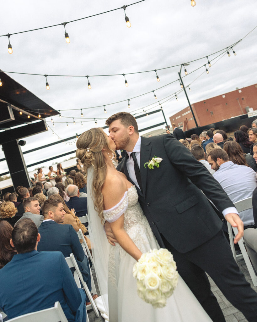 Bride and grooms end of aisle kiss after their rooftop patio wedding ceremony at Port 393 in Holland, Michigan.