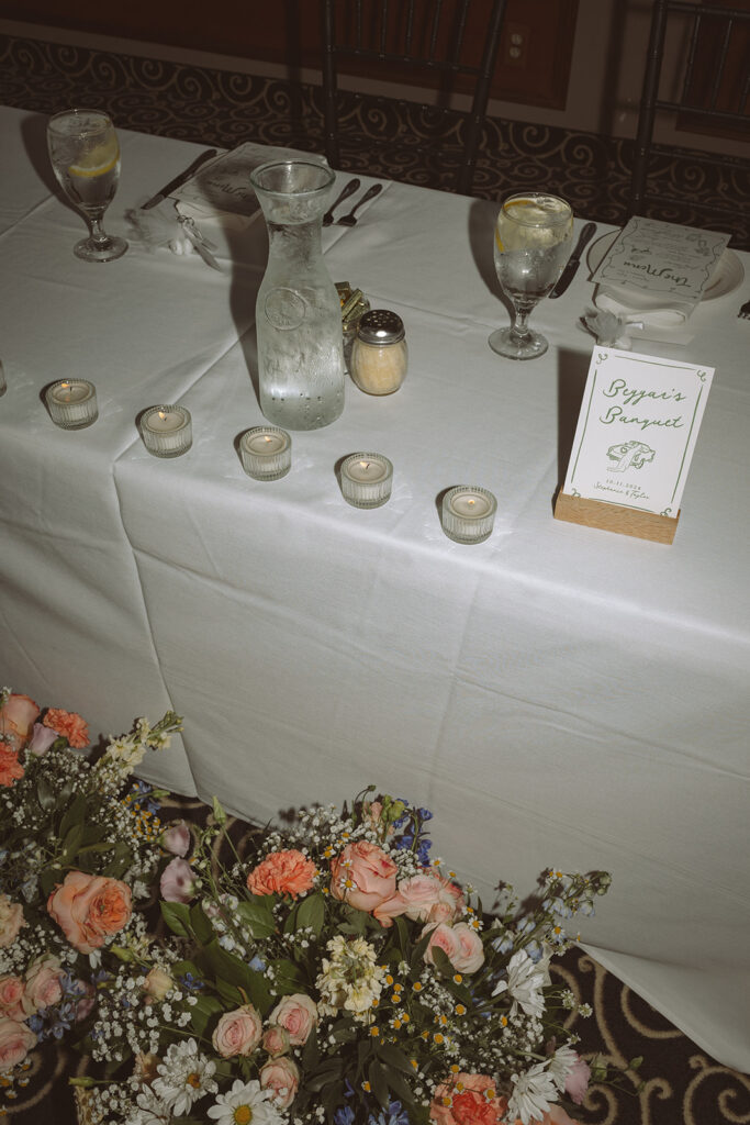 Close-up of table details with water carafe, votive candles, and custom sign during wedding reception