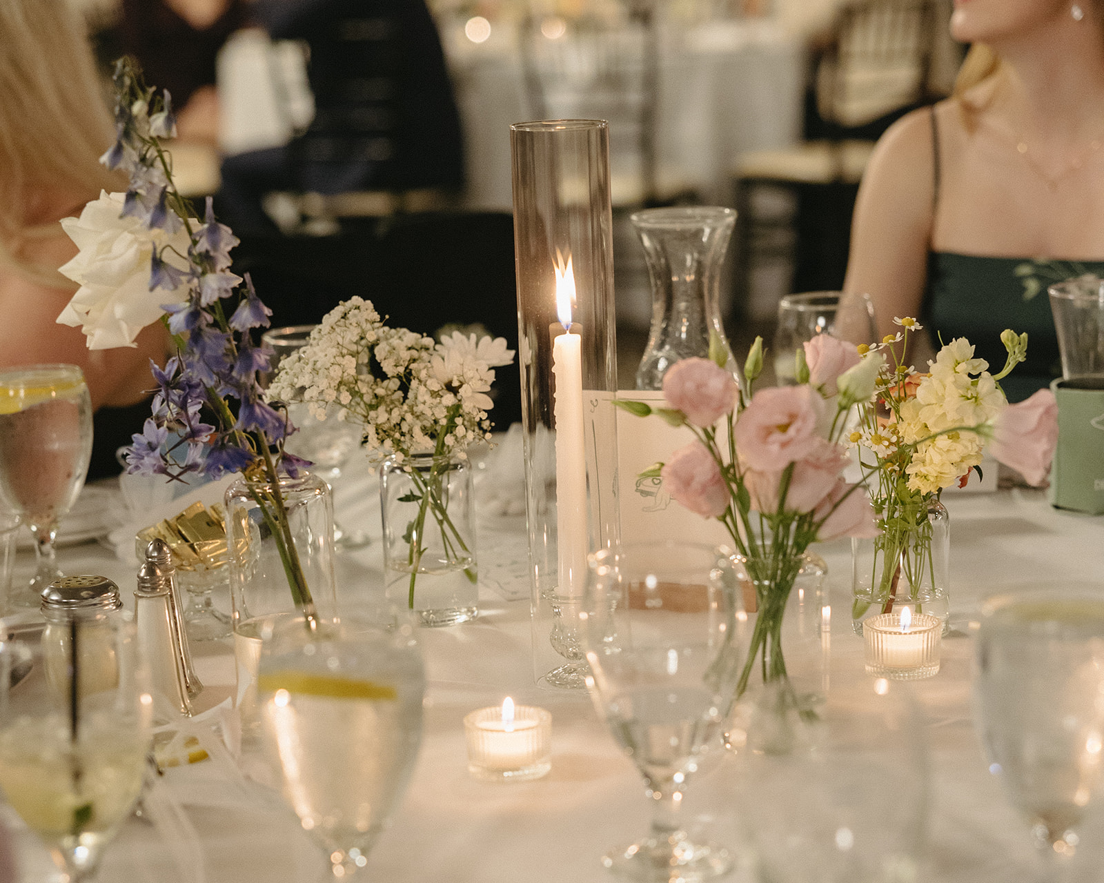 Close-up of candlelight and wildflower centerpieces in glass vases at reception dinner tables