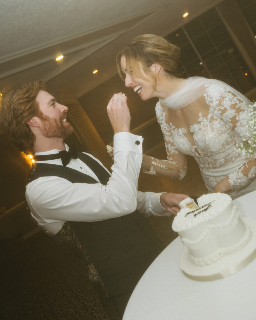 Bride and groom laughing while feeding each other cake during their Pine Knob Mansion wedding reception